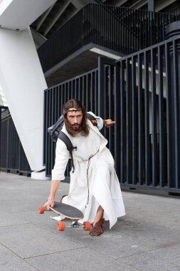 bornoz ve sokakta longboard üzerinde paten dikenli taç ciddi İsa