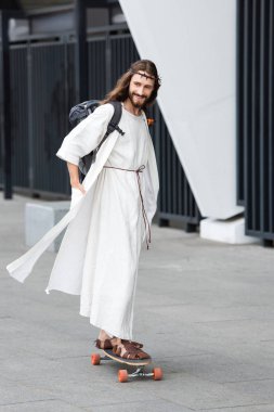 bornoz ve sokakta longboard üzerinde paten dikenli taç İsa gülümseyerek 