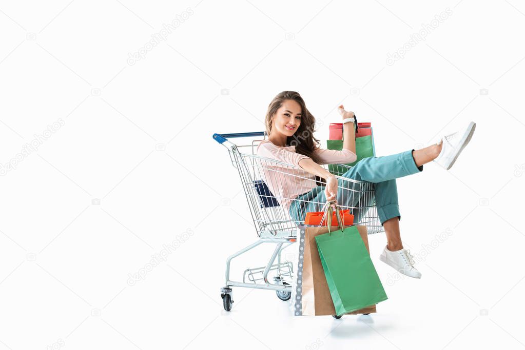 happy beautiful girl sitting in shopping cart with bags, isolated on white