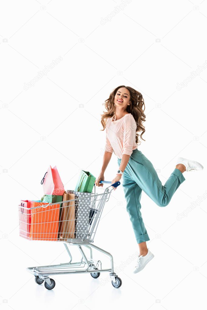 beautiful cheerful girl jumping with shopping cart and bags, isolated on white