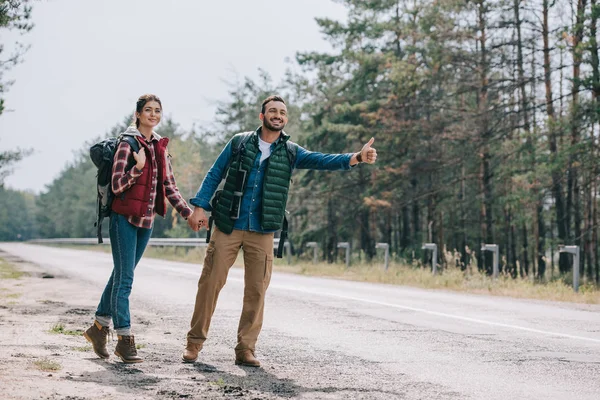 Pareja Viajeros Con Mochilas Cogidas Mano Mientras Hacen Autostop Carretera — Foto de Stock