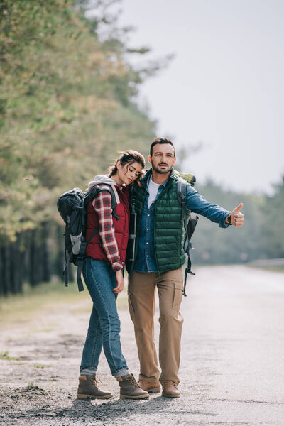 couple of travelers with backpacks hitchhiking on road