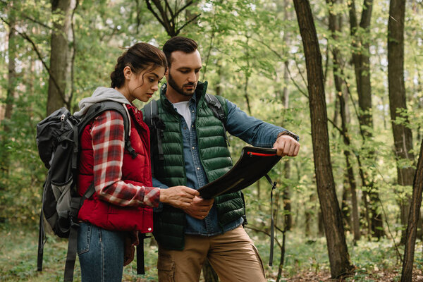 man and woman looking for destination on map while hiking in forest together