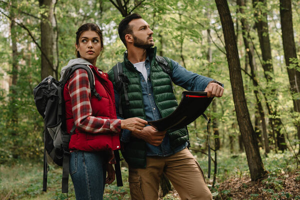 man and woman looking for destination on map while hiking in forest together