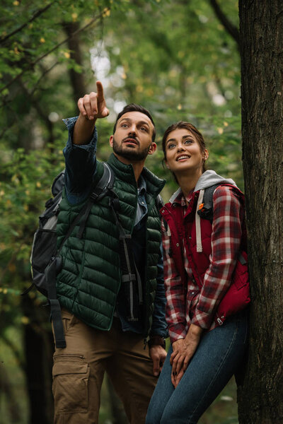 portrait of man and woman with backpacks looking away while hiking in woods