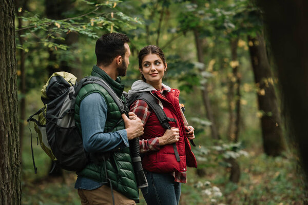 side view of man and woman with backpacks hiking in woods