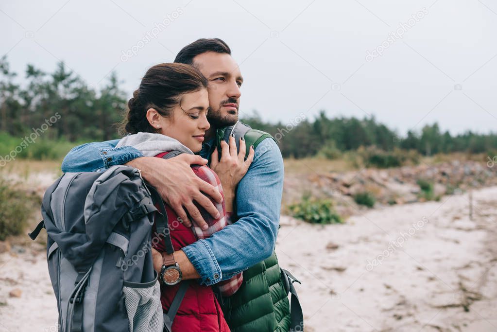 couple of hikers with backpacks hugging on sandy beach