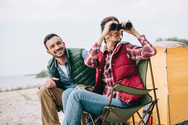 couple with binoculars resting on chairs on camping