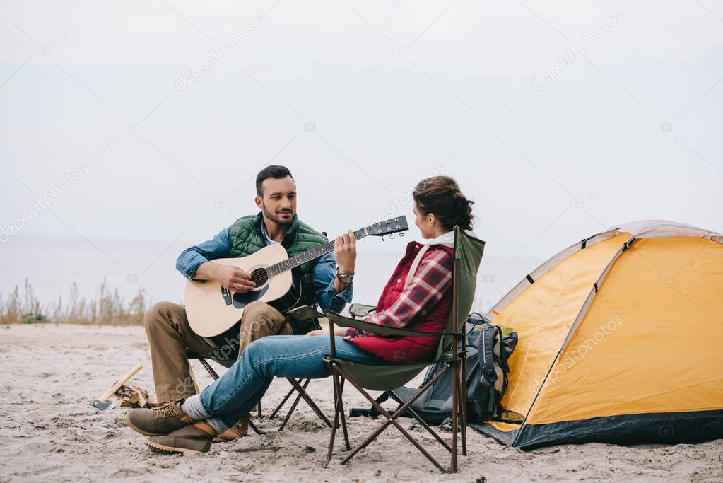 man playing acoustic guitar for wife on camping