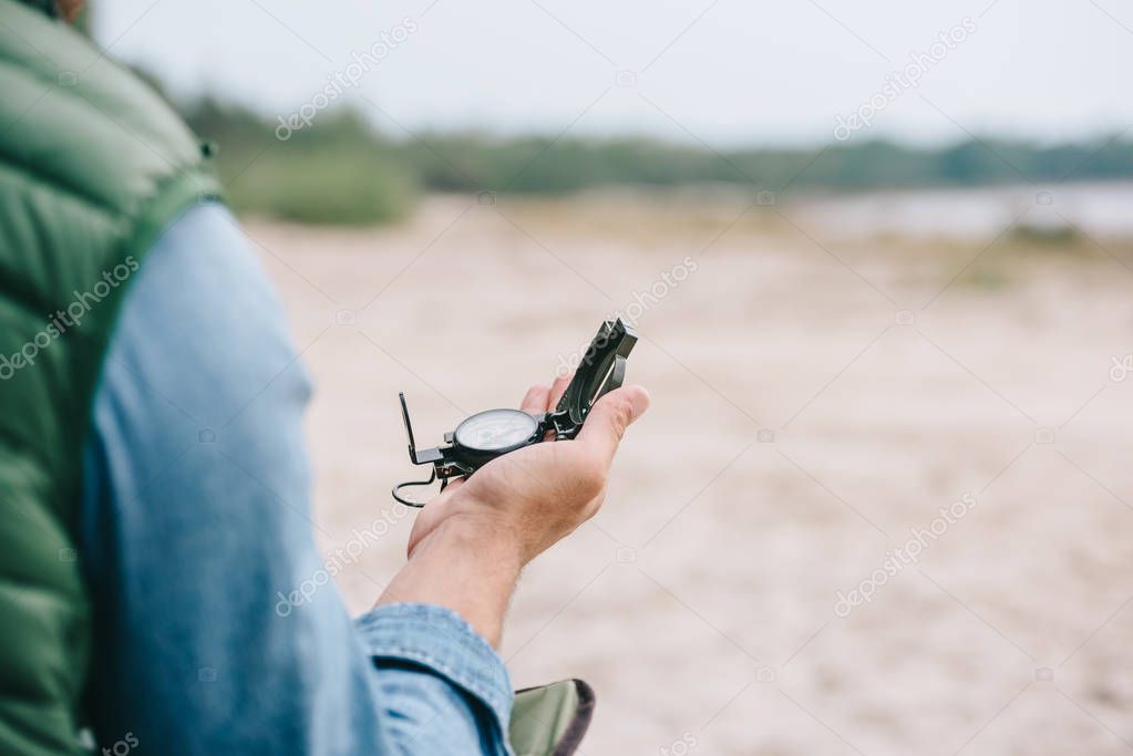 partial view of traveler holding compass in hand