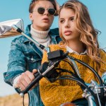 Young couple sitting on motorbike against blue sky