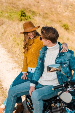 Retro motosiklet üzerinde oturan ve kırsal çayır üzerinde birbirine bakarak şık çift