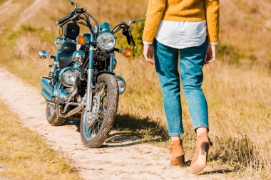Genç kadın vintage motosiklet yakınındaki izi boyunca yürüyüş görünümünü kırpılmış