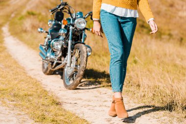 Genç kadın izi retro motosiklet yakınındaki boyunca yürüyüş görünümünü kırpılmış