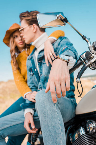 young couple sitting on retro motorbike on rural meadow