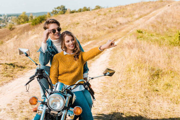happy couple sitting on motorbike and girlfriend showing something  