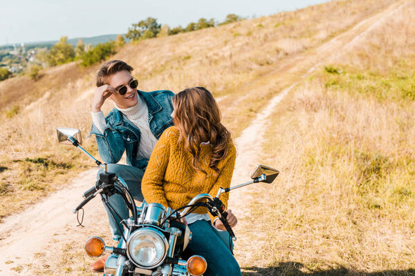 couple sitting on retro motorbike and looking at each other