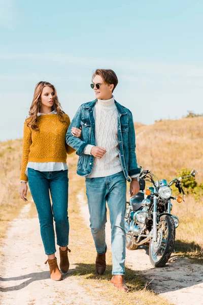 バイク近く田舎の牧草地の上を歩いて笑顔のカップル — ストック写真