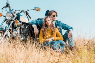 Genç erkek ve kız arkadaşı yakınındaki motosiklet çayır üzerinde otururken