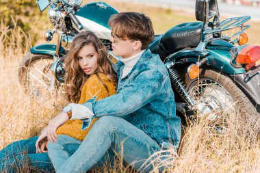 young couple sitting near vintage motorbike on meadow clipart
