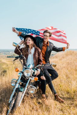 motosiklet, bağımsızlık günü kavramı üzerinde oturan Amerikan bayrağı ile gülümseyen çift  