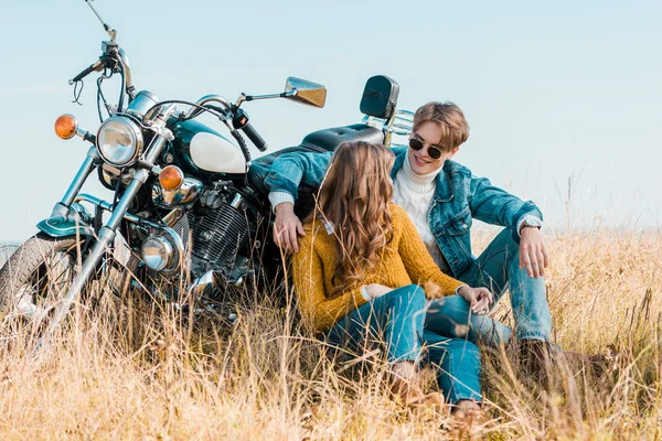 young couple sitting near vintage motorbike