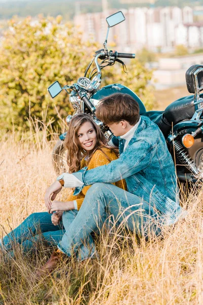 young couple sitting near vintage motorbike and looking at each other