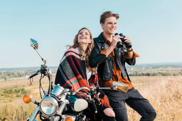 バイクの上に座ってのガール フレンドの近くの双眼鏡を持って笑顔の彼氏 — ストック写真