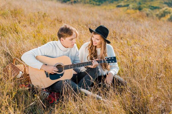 young man playing guitar while woman smiling on meadow