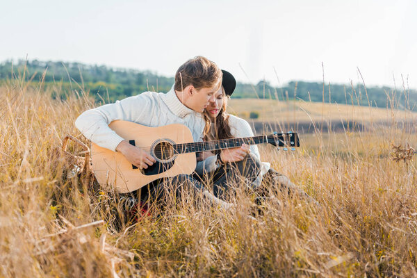 парень играет на гитаре рядом с девушкой на сельском лугу
