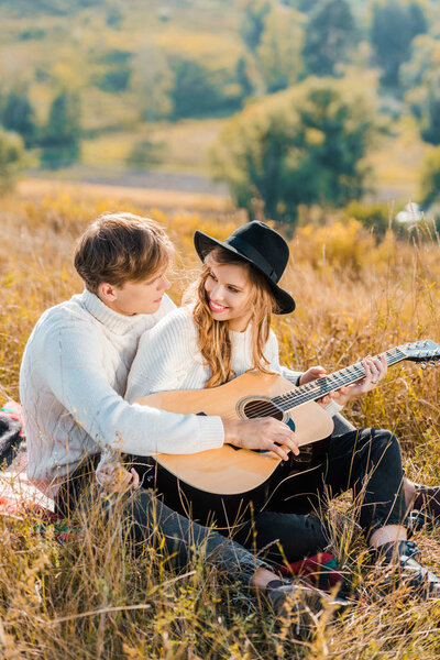 улыбающаяся пара, играющая на гитаре и отдыхающая на лугу
