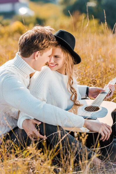smiling couple looking at each other while young man holding guitar