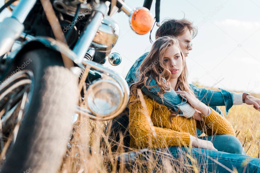 boyfriend hugging girlfriend and sitting near vintage motorbike