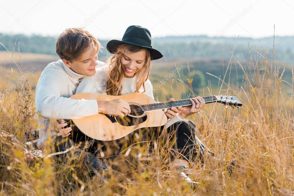 happy couple playing guitar on rural meadow