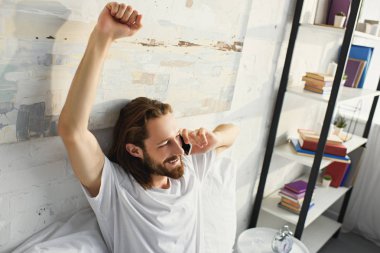 streç yapıyor ve smartphone yatağa evde sabah zaman sırasında konuşan uzun saçlı sakallı adamın yüksek açılı görünüş