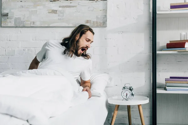 Zívající Mladík Dlouhosrstý Probuzení Posteli Budík Doma — Stock fotografie