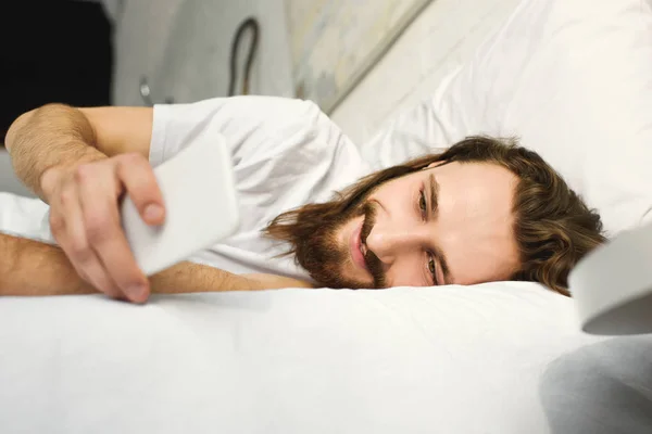 Uomo Barbuto Sorridente Con Capelli Lunghi Utilizzando Smartphone Letto Durante — Foto Stock