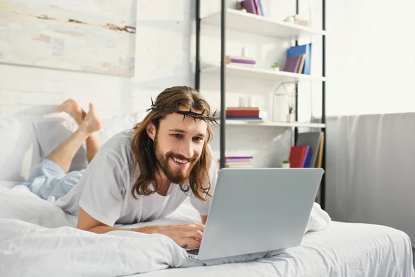 smiling Jesus using laptop in bed during morning time at home