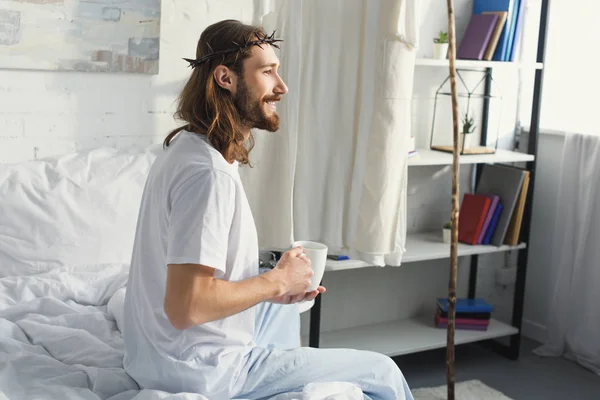 side view of Jesus in crown of thorns drinking coffee in bedroom during morning time at home