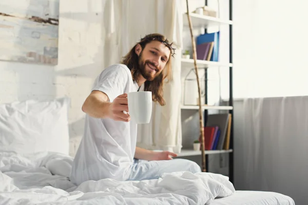 selective focus of Jesus in crown of thorns showing coffee cup in bedroom at home