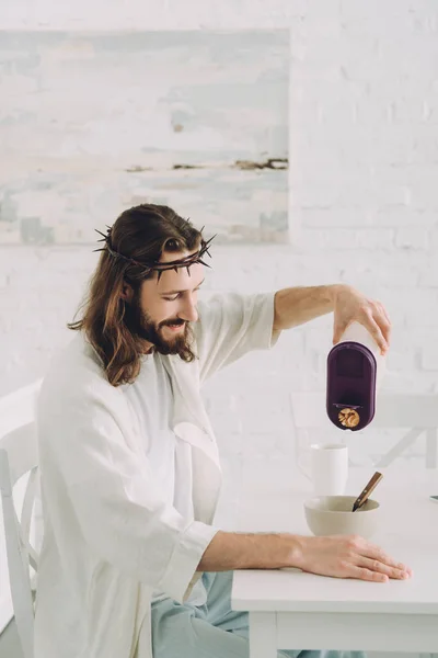 快乐的耶稣把玉米片倒入碗里 放在厨房的餐桌上 — 图库照片