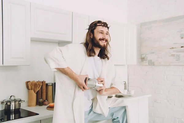 smiling Jesus grinding coffee beans with hands in manual coffeemill in kitchen at home