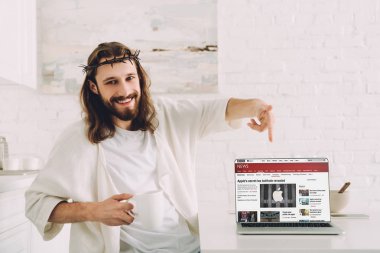 kahve tutarak ve bbc haber sitesi evde mutfak ile laptop işaret neşeli İsa