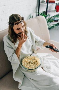 İsa'nın yüksek açı görünümünde tv izlerken, evde kanepenin üzerinde patlamış mısır yemek dikenli taç