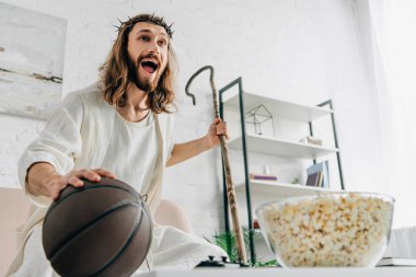 evde kanepe üzerinde ahşap personel holding topu ve izlerken basketbol maçı ile heyecanlı İsa'nın düşük açılı görünüş