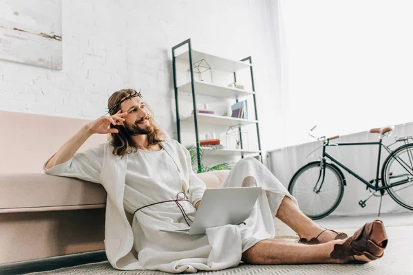 dreamy Jesus sitting on floor and using laptop near sofa at home