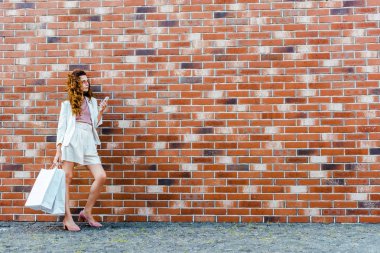 Alışveriş torbaları tuğla duvar önünde smartphone kullanarak olan şık kadın
