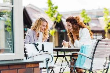 happy young women sitting in cafe together after shopping clipart