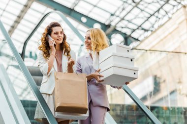 güzel genç kadınlarla alışveriş torbaları ve alışveriş merkezinde yürüyen merdiven kutusu