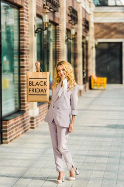 beautiful stylish woman holding shopping bag with black friday sign and looking up at mall clipart